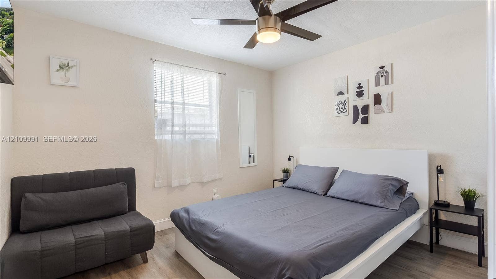 Neutral-toned room featuring wood-finish flooring, a ceiling fan with integrated lighting, and a single window