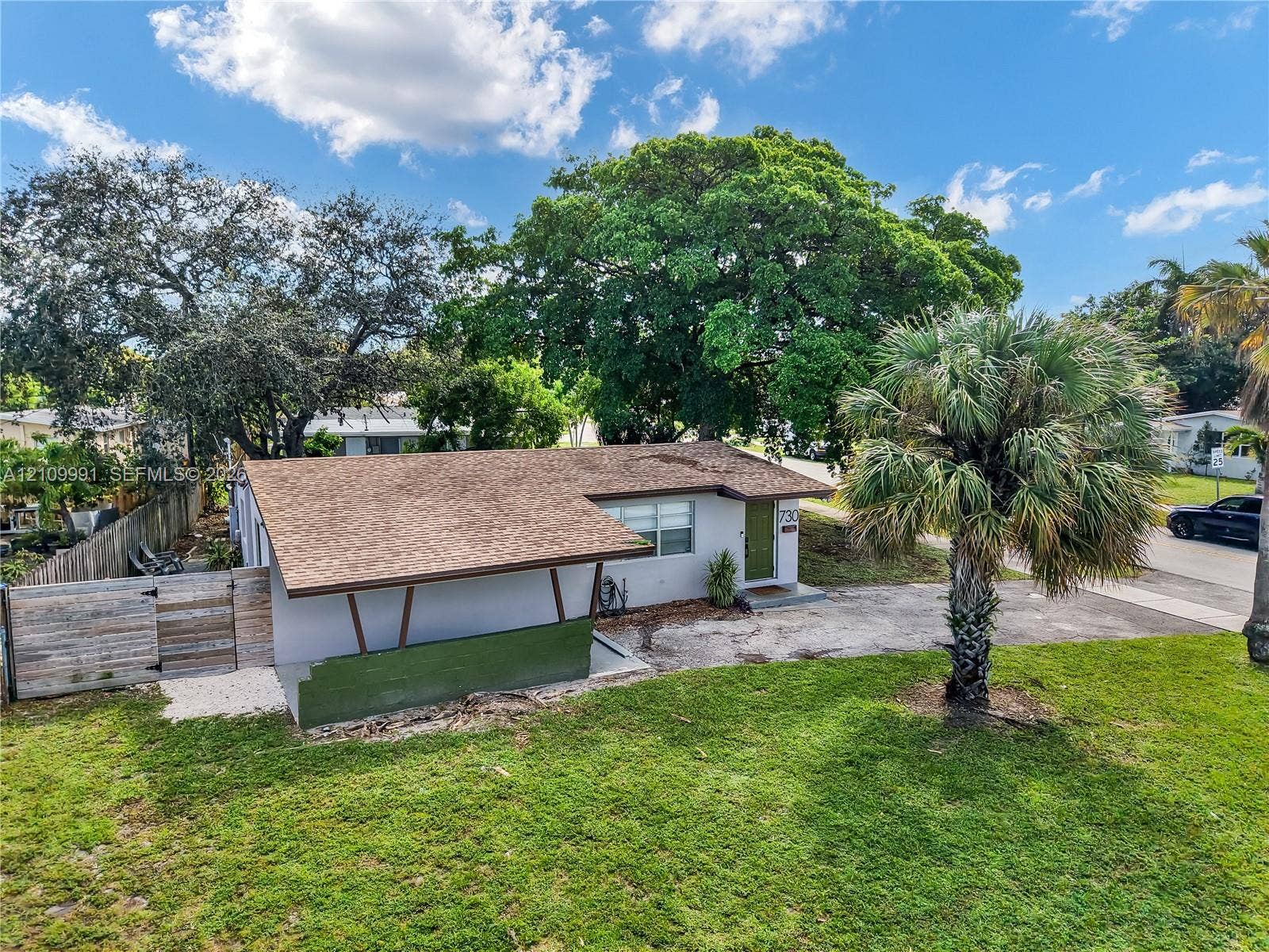 Single-story residence featuring an asphalt shingle roof, a carport with angled structural supports, mature landscaping, and a wood privacy fence