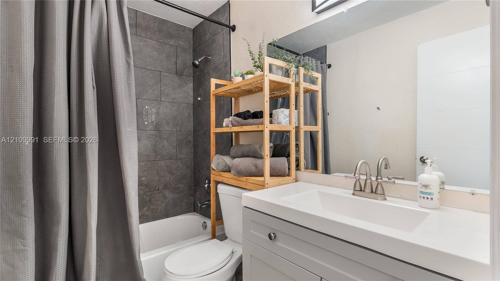 Bathroom featuring a gray vanity with a white countertop and integrated sink, a large wall-mounted mirror, and a tub-shower surround finished with large-format gray tile