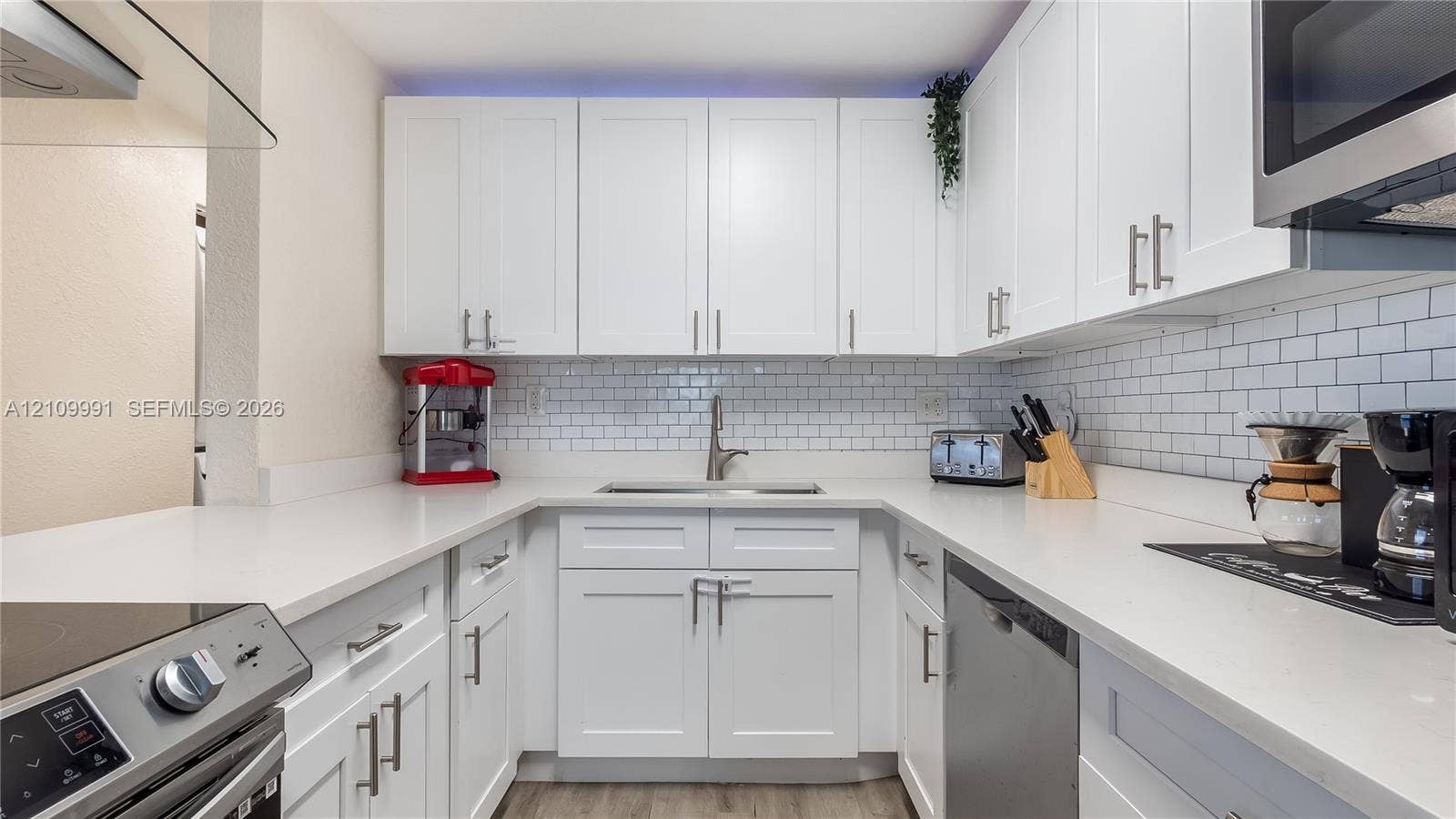 Kitchen featuring white Shaker-style cabinetry, solid-surface countertops, subway tile backsplash, stainless steel appliances, and under-cabinet lighting
