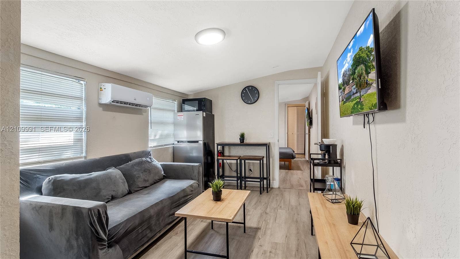 Interior space featuring wood-finish flooring, a wall-mounted ductless mini-split air conditioning unit, and aluminum-frame windows with horizontal blinds