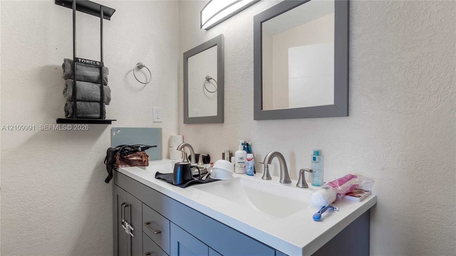 Bathroom vanity featuring shaker-style cabinetry, solid-surface countertop with an integrated sink, dual wall-mounted framed mirrors, and brushed-finish widespread faucets