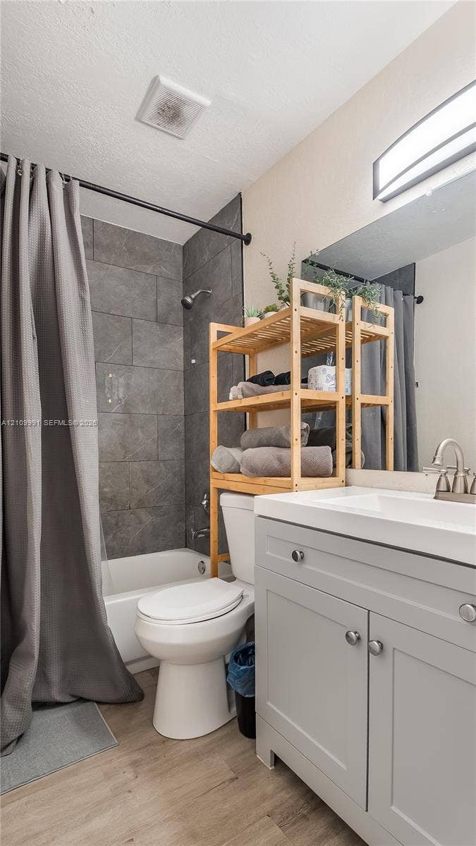 Light gray cabinetry with brushed metal hardware, white countertop, integrated sink with arched faucet, rectangular tile shower surround, and wood-finish flooring
