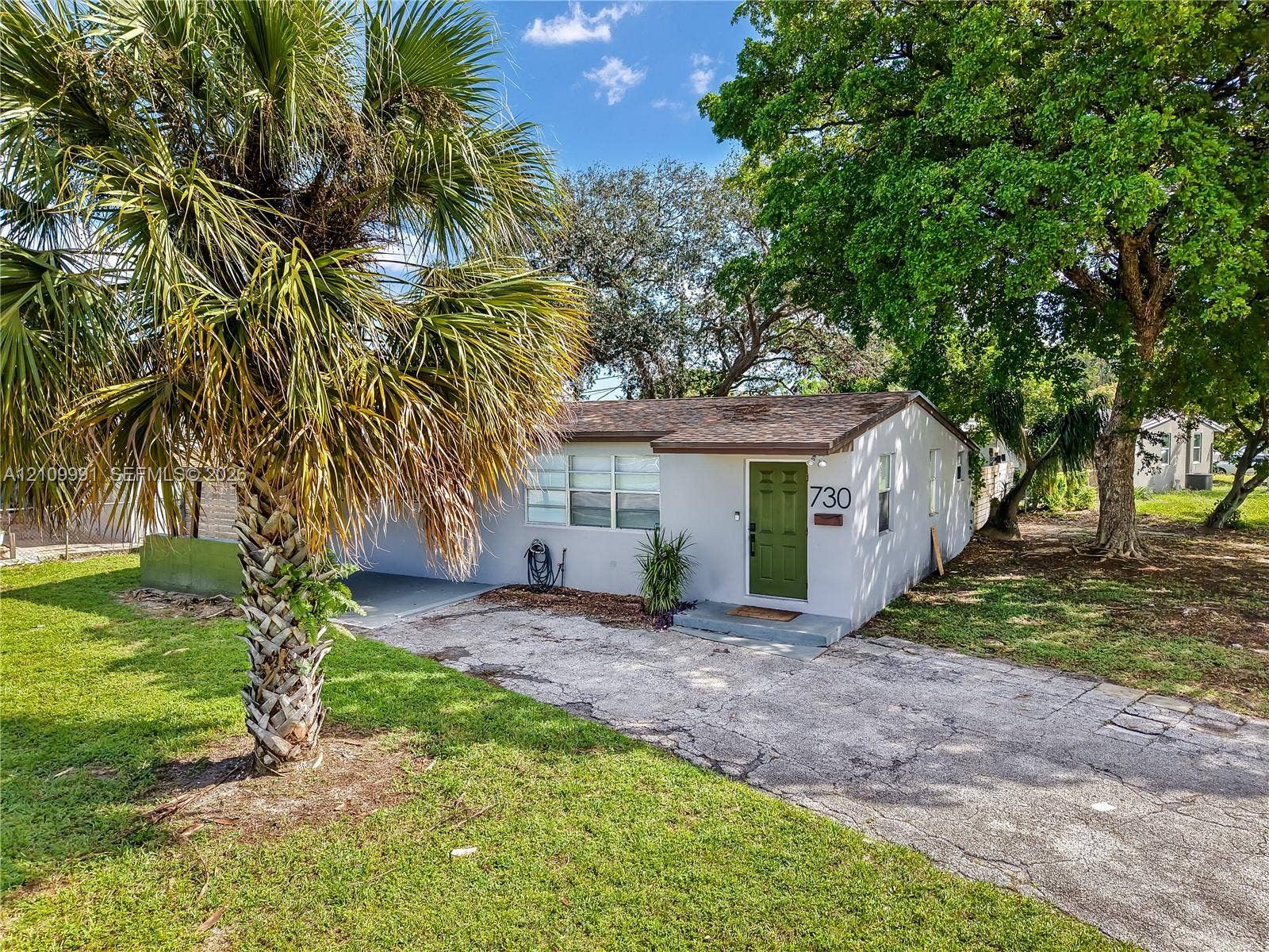Single-story residence featuring a painted stucco exterior, a shingled roof, a paved driveway, and established trees