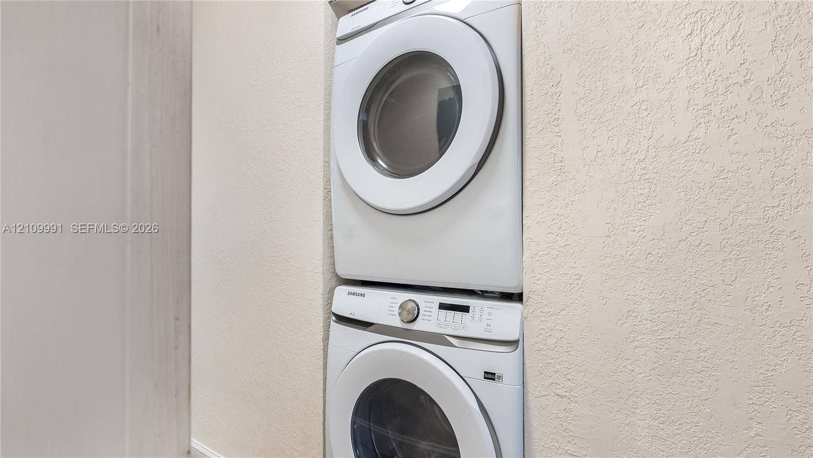 Stacked white washer and dryer unit housed within a recessed wall cavity