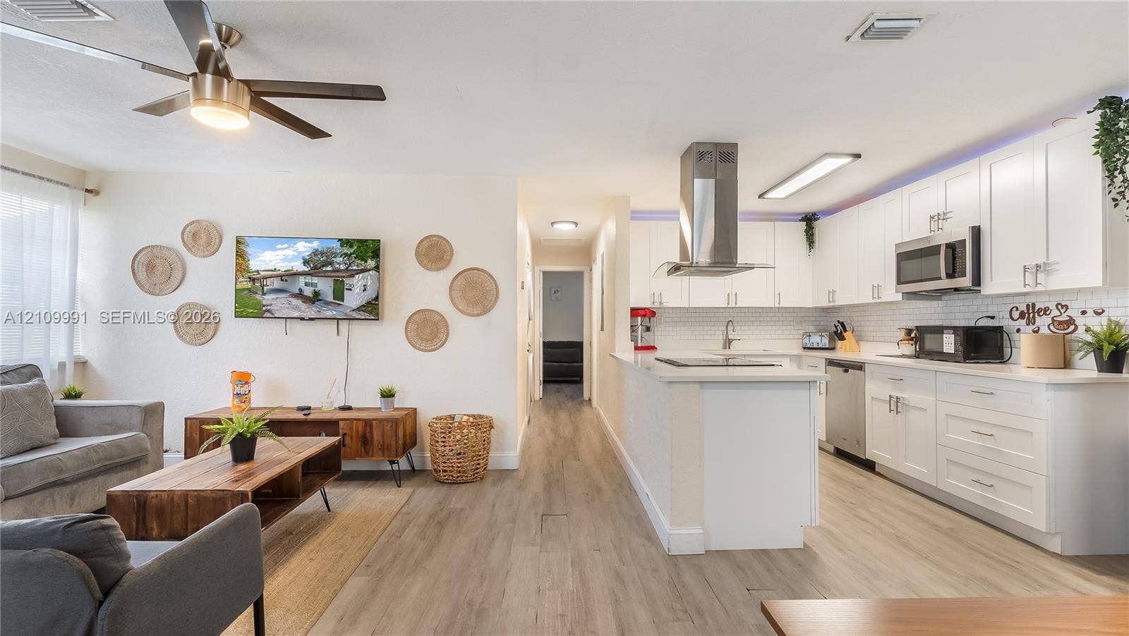 Open-concept kitchen featuring white shaker-style cabinetry, stainless steel appliances, a peninsula with stone-surface countertops, a stainless steel chimney-style range hood, and wood-finish flooring throughout