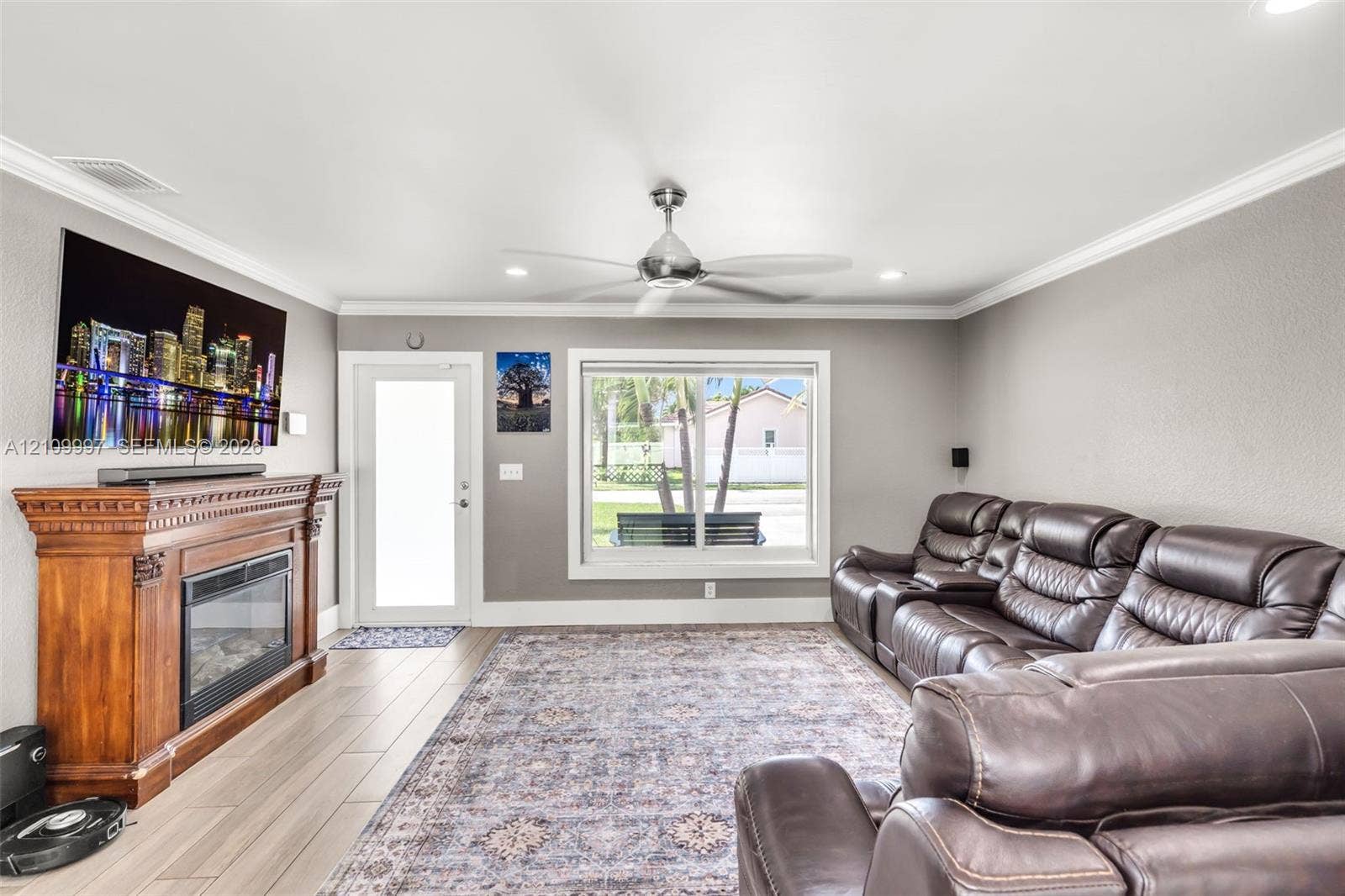 Living area featuring wood-finish flooring, a wood-mantel fireplace with a glass-front insert, recessed ceiling lighting, and a multi-blade ceiling fan