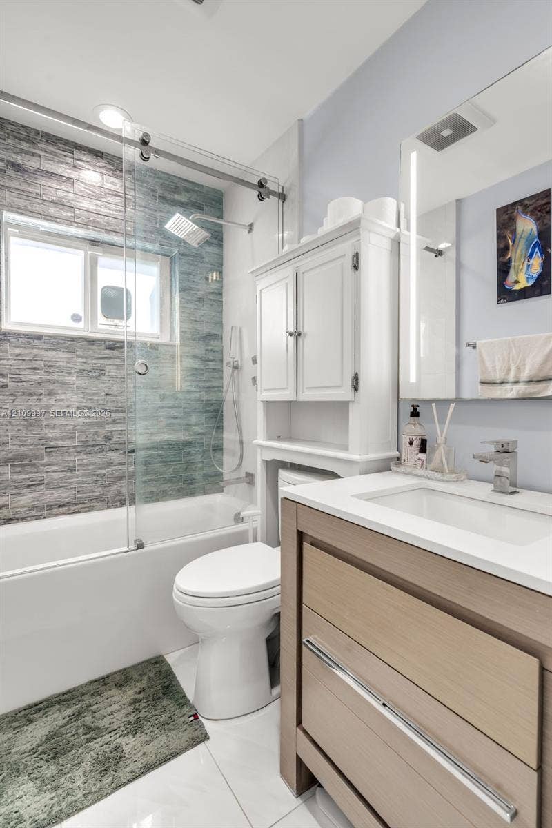 Bathroom featuring a wood-finish vanity with a white countertop, glass-enclosed shower with horizontal tile surround, wall-mounted cabinet, and integrated mirror lighting