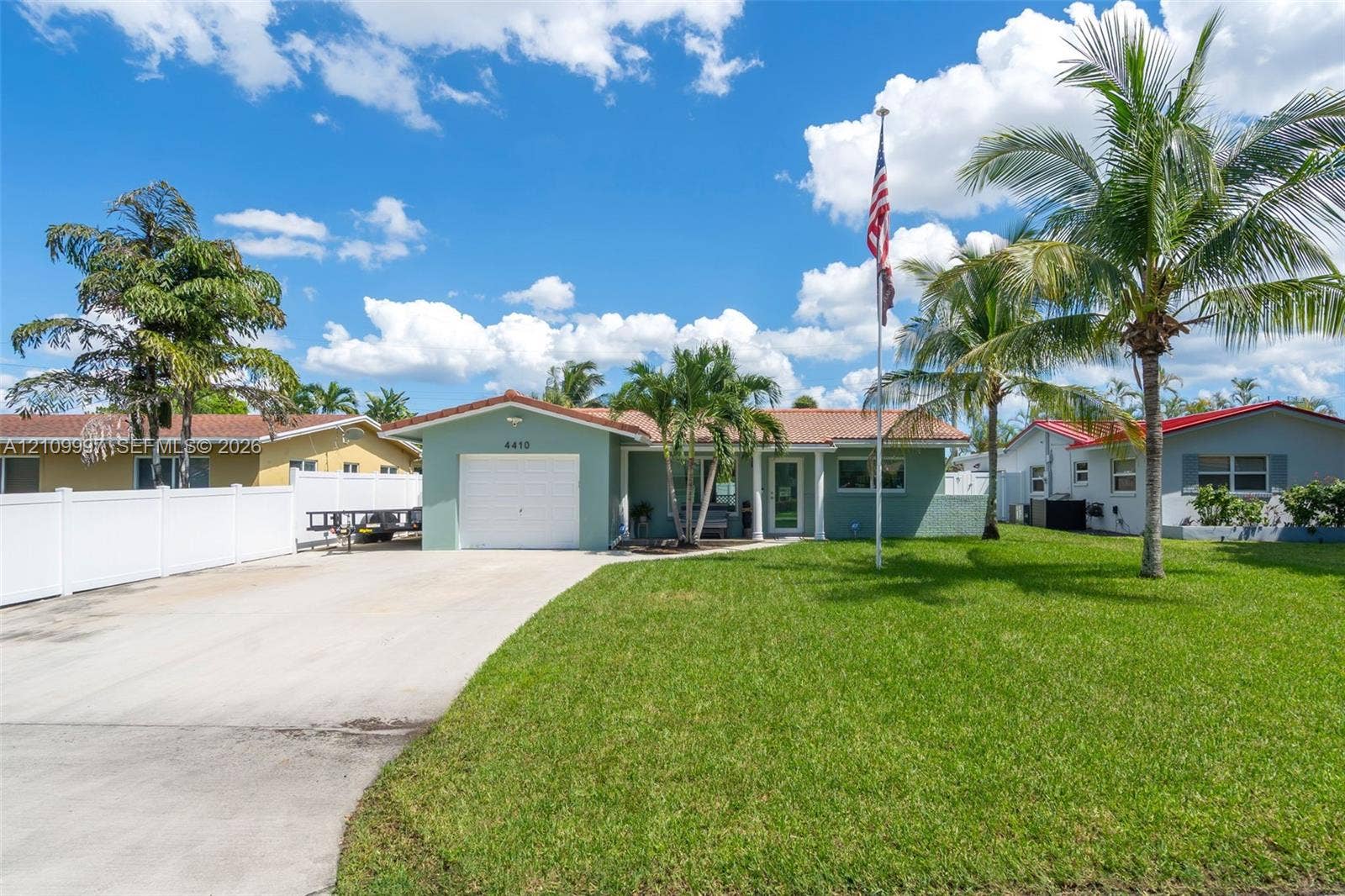 Single-story residence featuring a concrete tile roof, attached one-car garage, concrete driveway, and white vinyl privacy fencing