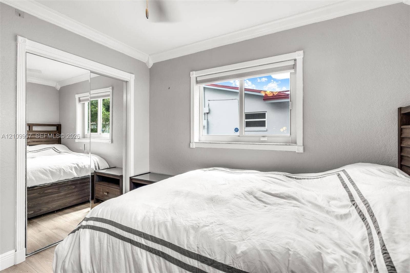 Room featuring neutral paint, crown molding, wood-finish flooring, and a sliding mirrored closet door