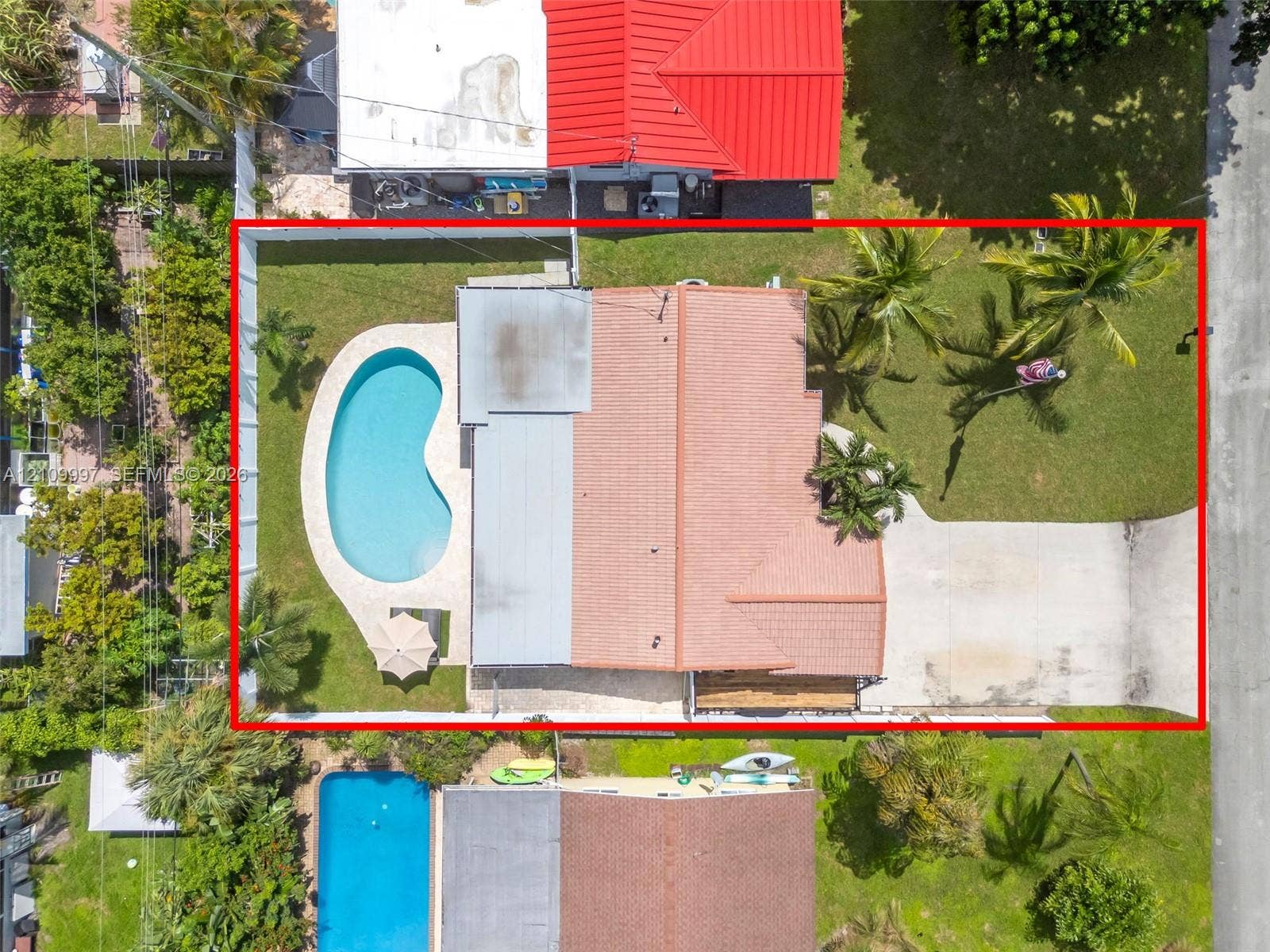 Aerial perspective of property featuring an in-ground swimming pool, concrete driveway, tiled roof, and landscaped lawn with mature palm trees