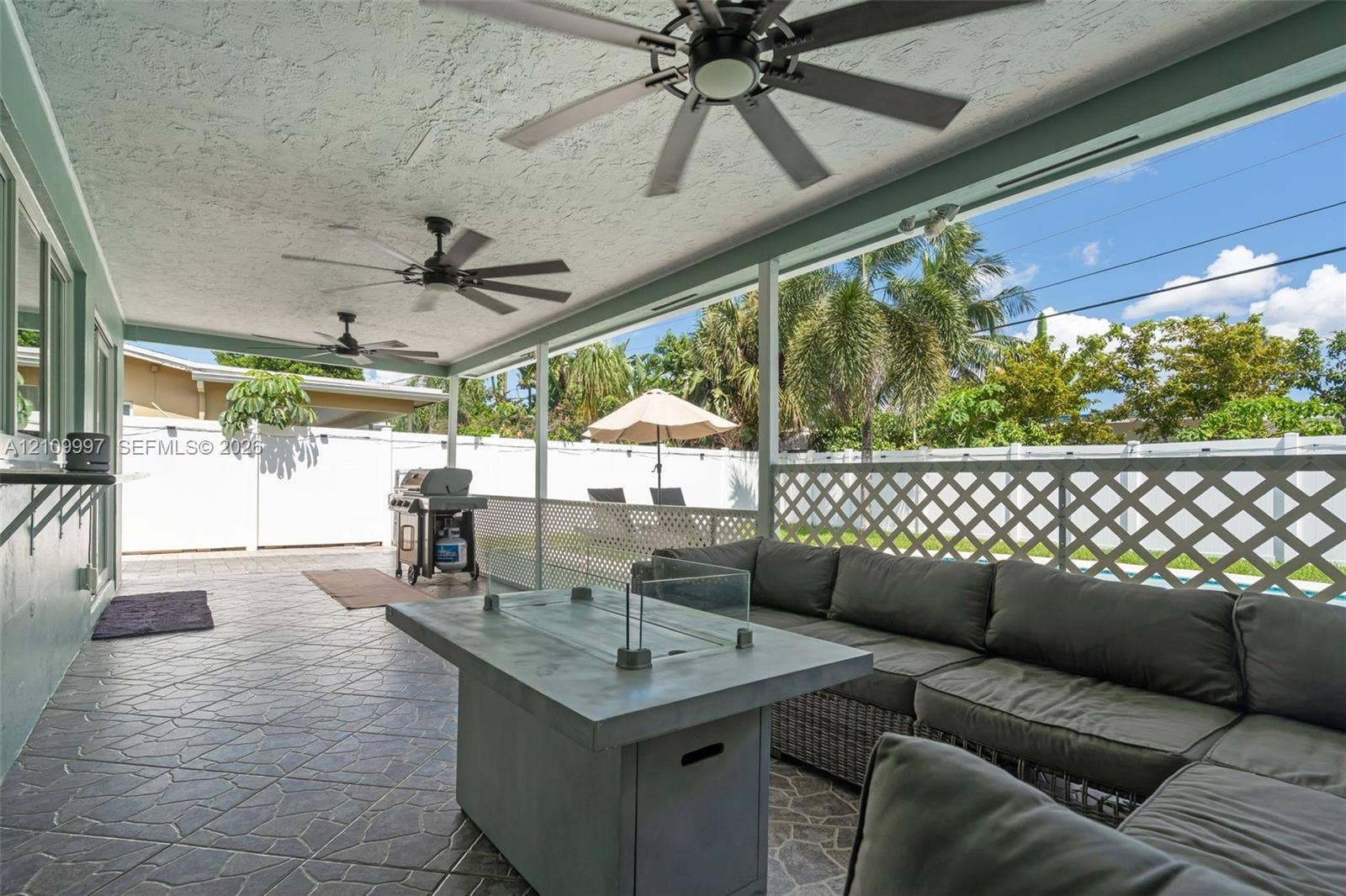 Covered patio featuring stone-patterned flooring, dual ceiling fans, and white lattice privacy fencing