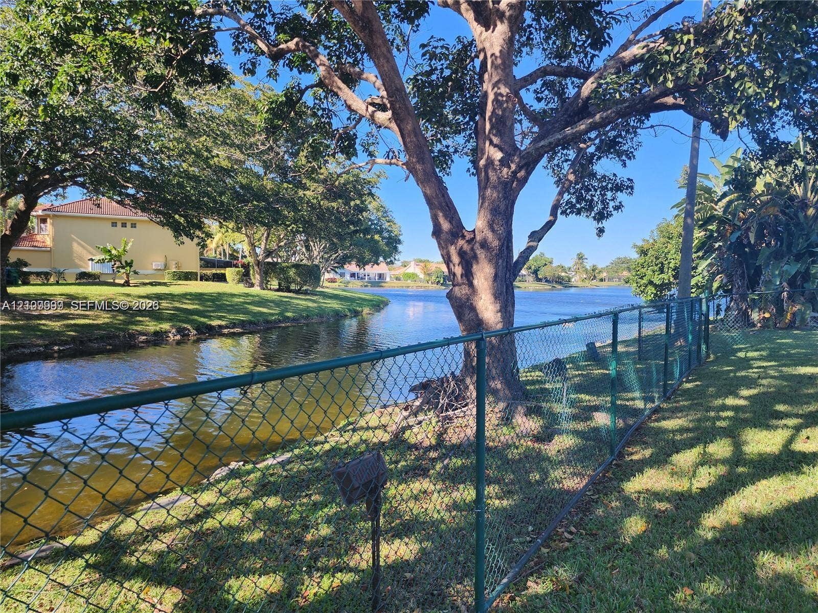 1794 NW 112th Terrace, Coral Springs, Coral Springs, FL 33071 Waterfront lot featuring mature trees, a chain-link perimeter fence, and grass landscaping