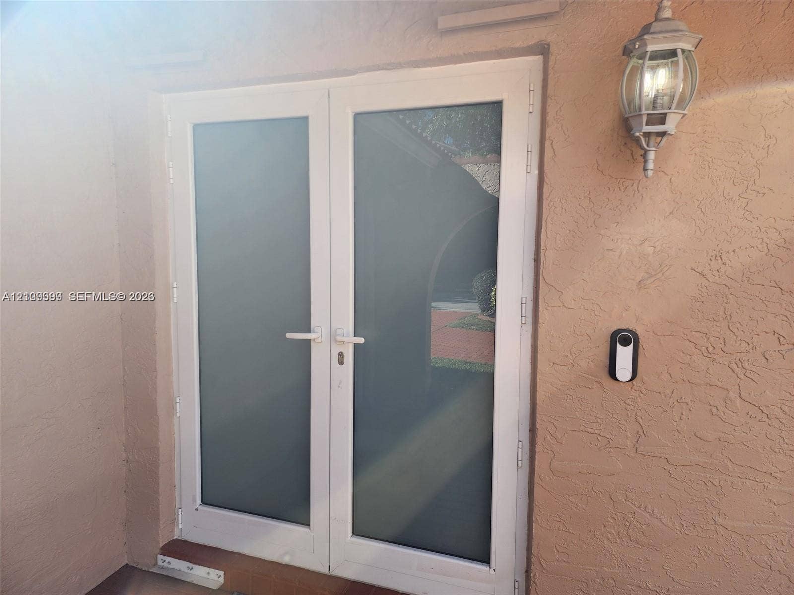 1794 NW 112th Terrace, Coral Springs, Coral Springs, FL 33071 Double glass-panel doors with white frames, textured stucco exterior wall, and traditional wall-mounted lantern-style fixture