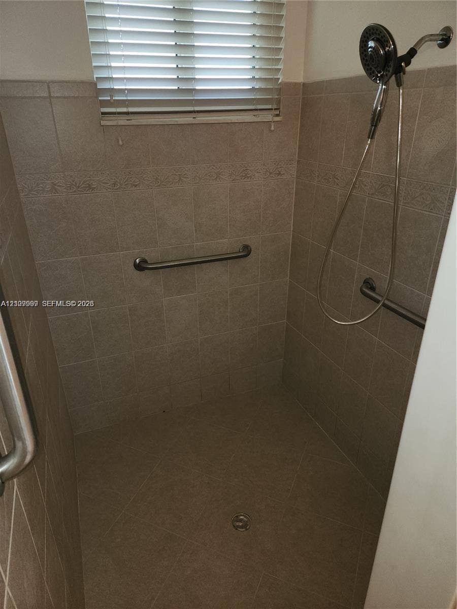 1794 NW 112th Terrace, Coral Springs, Coral Springs, FL 33071 Walk-in shower featuring neutral tile walls, horizontal accent tiling, stainless steel grab bars, and an adjustable handheld showerhead
