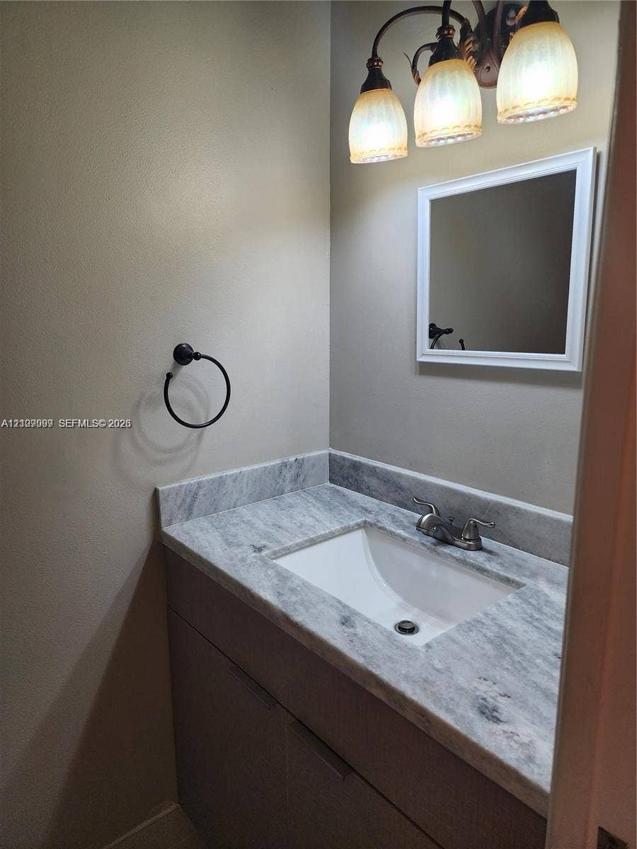 1794 NW 112th Terrace, Coral Springs, Coral Springs, FL 33071 Vanity featuring a stone-surface countertop with an integrated rectangular sink, three-light decorative fixture, framed mirror, and matte black towel ring
