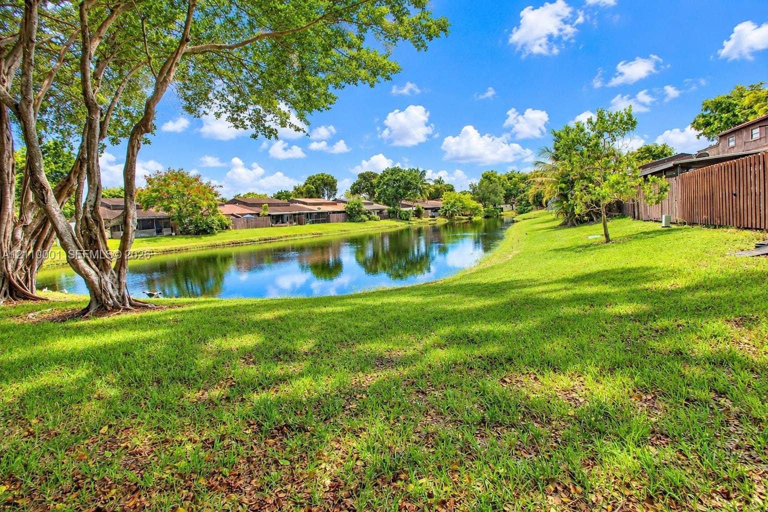 3617 SW 69th Terrace, #24-Z, Miramar, FL 33023 Waterfront property featuring a landscaped lawn, mature trees, and a wooden privacy fence