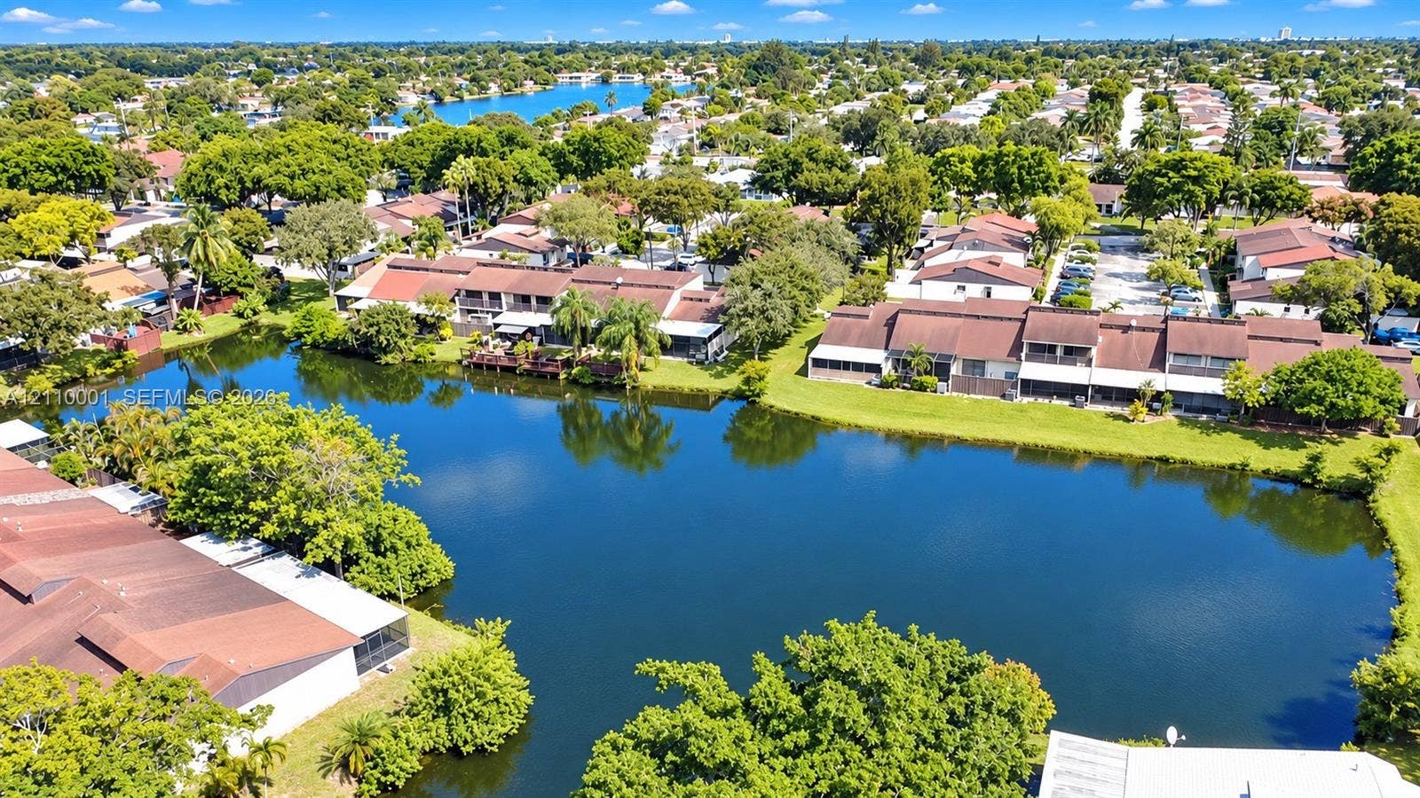 3617 SW 69th Terrace, #24-Z, Miramar, FL 33023 Aerial perspective showcasing expansive water frontage with mature trees, manicured lawns, and multi-level residential structures featuring shingled roofs and enclosed patios