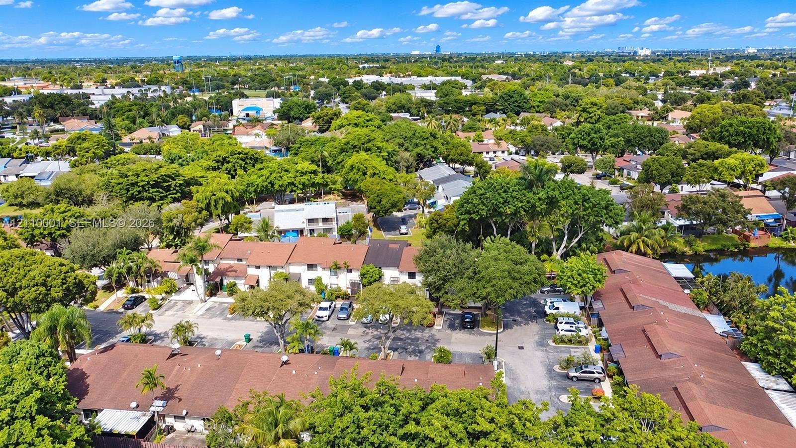 3617 SW 69th Terrace, #24-Z, Miramar, FL 33023 Aerial perspective featuring multiple multi-unit buildings with shingle roofing, paved surface parking, mature canopy trees, and an integrated waterfront pond