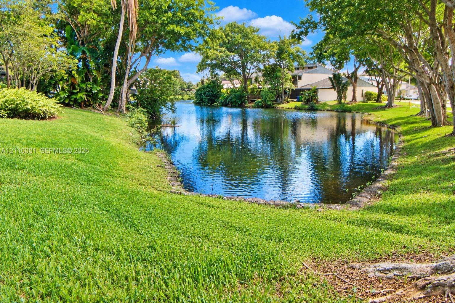 3617 SW 69th Terrace, #24-Z, Miramar, FL 33023 Waterfront lot featuring a manicured lawn, stone-lined pond edge, and mature trees