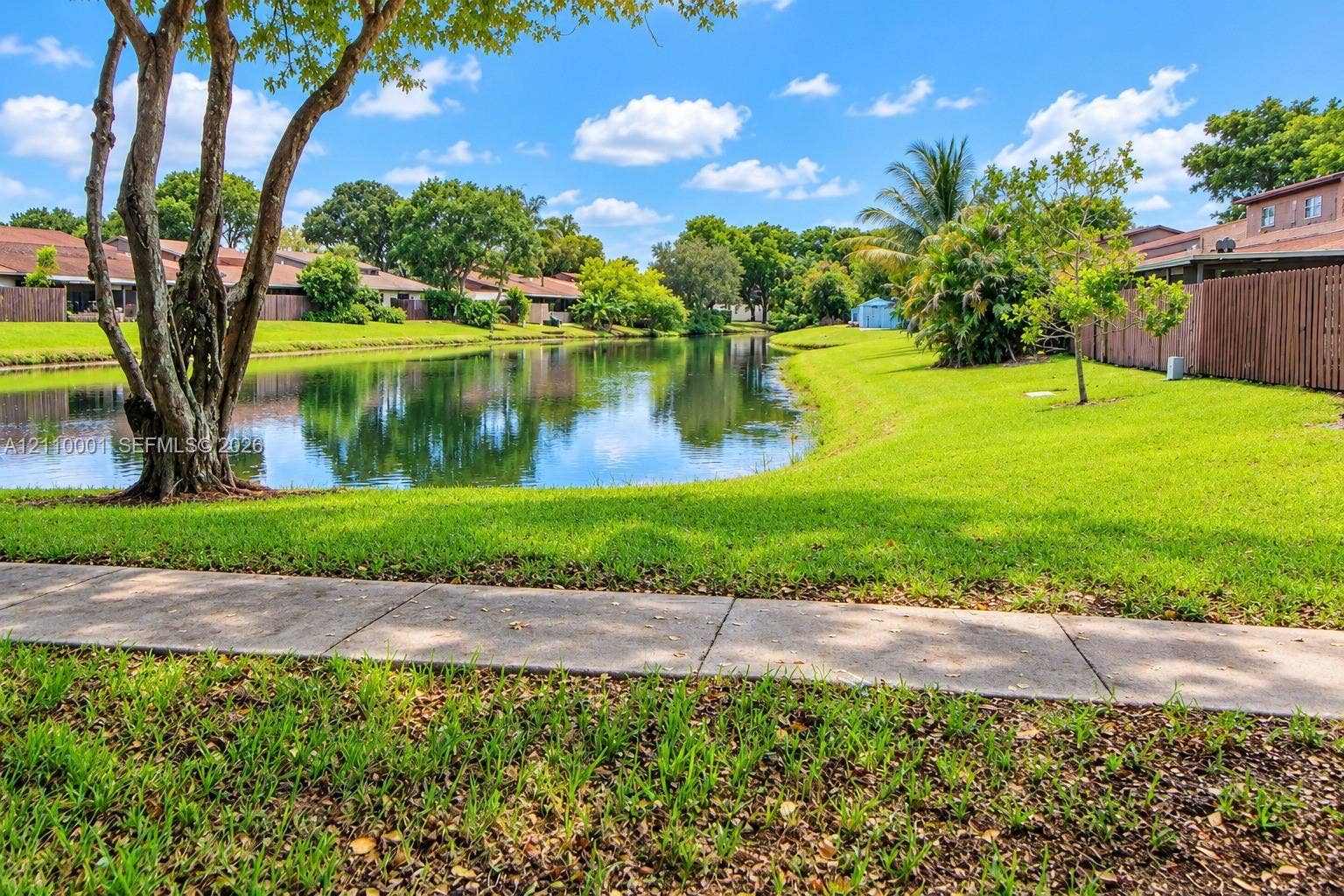 3617 SW 69th Terrace, #24-Z, Miramar, FL 33023 Waterfront grounds featuring a concrete walking path, mature trees, manicured lawn, and perimeter wood fencing