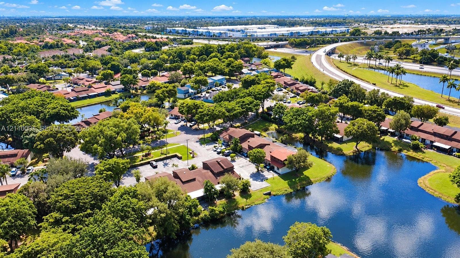3617 SW 69th Terrace, #24-Z, Miramar, FL 33023 Aerial perspective of a multi-unit residential complex featuring terracotta-tiled rooflines, expansive water features, mature canopy trees, and paved parking areas