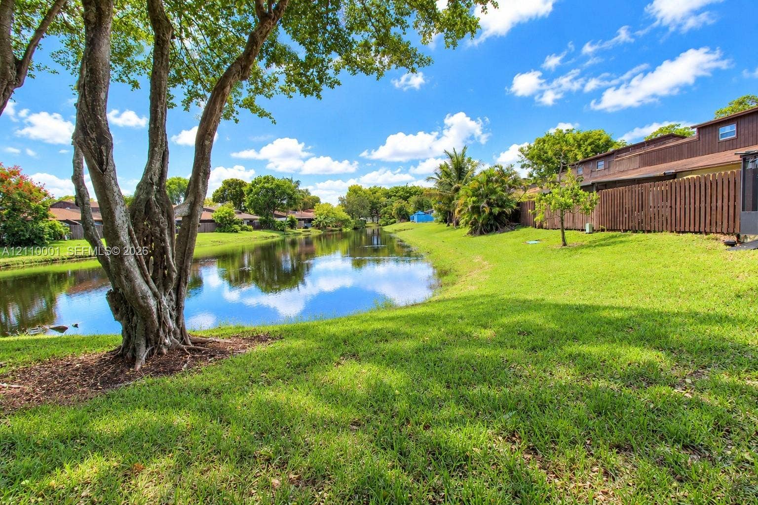3617 SW 69th Terrace, #24-Z, Miramar, FL 33023 Waterfront backyard featuring a manicured lawn, mature trees, and a wooden perimeter fence