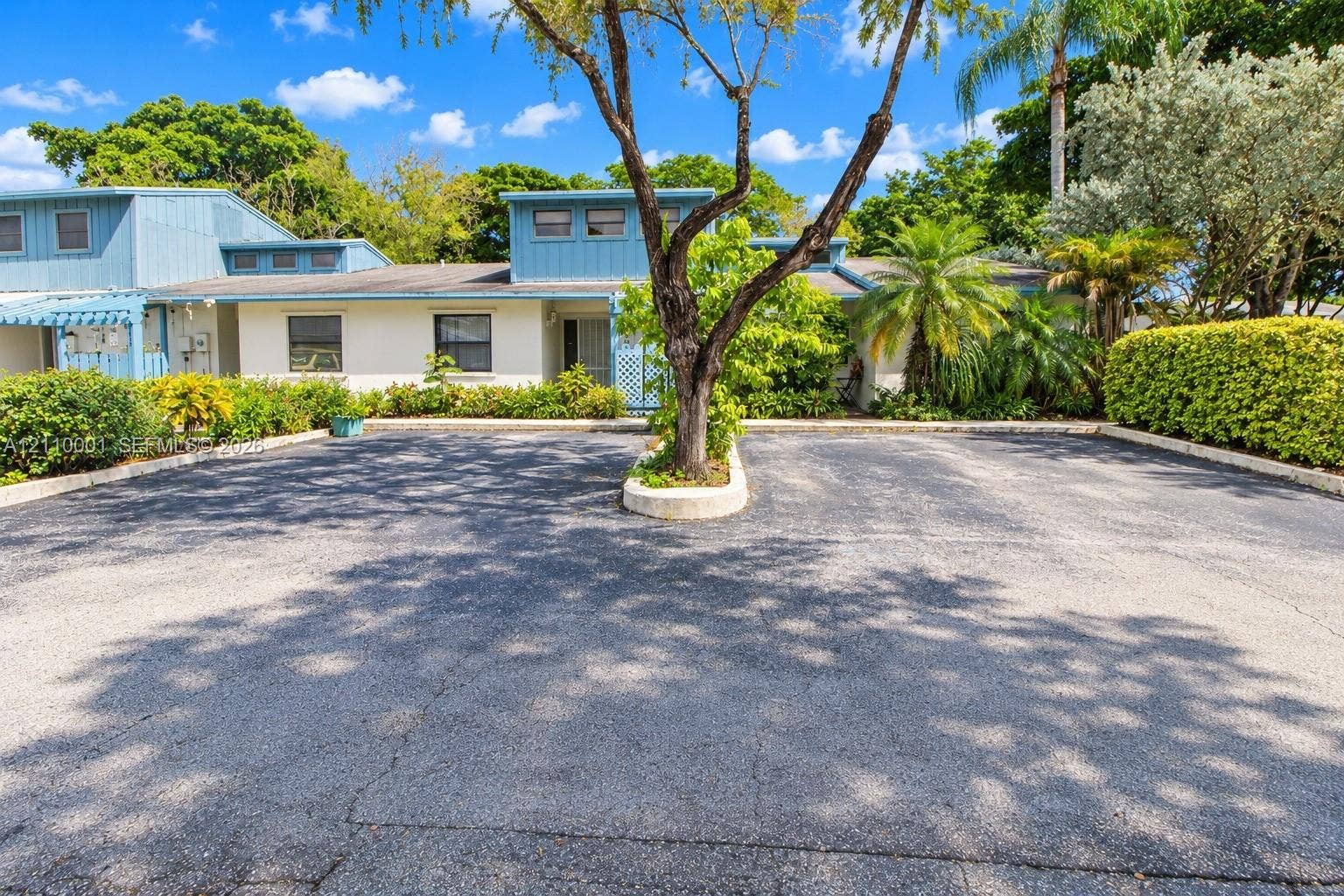 3617 SW 69th Terrace, #24-Z, Miramar, FL 33023 Exterior facade featuring a combination of horizontal siding and smooth stucco finish, asphalt paved parking area, central planter bed with mature tree, and surrounding lush landscaping