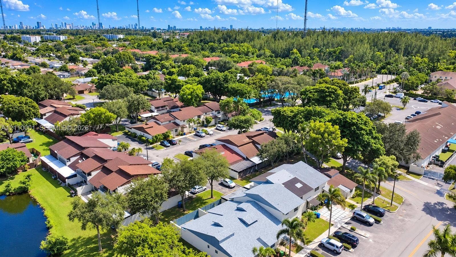 3617 SW 69th Terrace, #24-Z, Miramar, FL 33023 Aerial perspective of a multi-unit residential community featuring brown shingle roofs, paved parking areas, dense mature landscaping, and a water feature