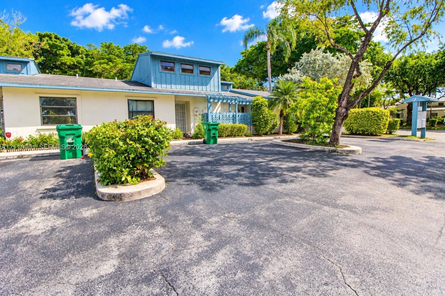 3617 SW 69th Terrace, #24-Z, Miramar, FL 33023 Single-story exterior featuring light-toned stucco siding, a blue-painted clerestory roofline, metal-framed windows, and an asphalt-paved lot with integrated landscaped islands