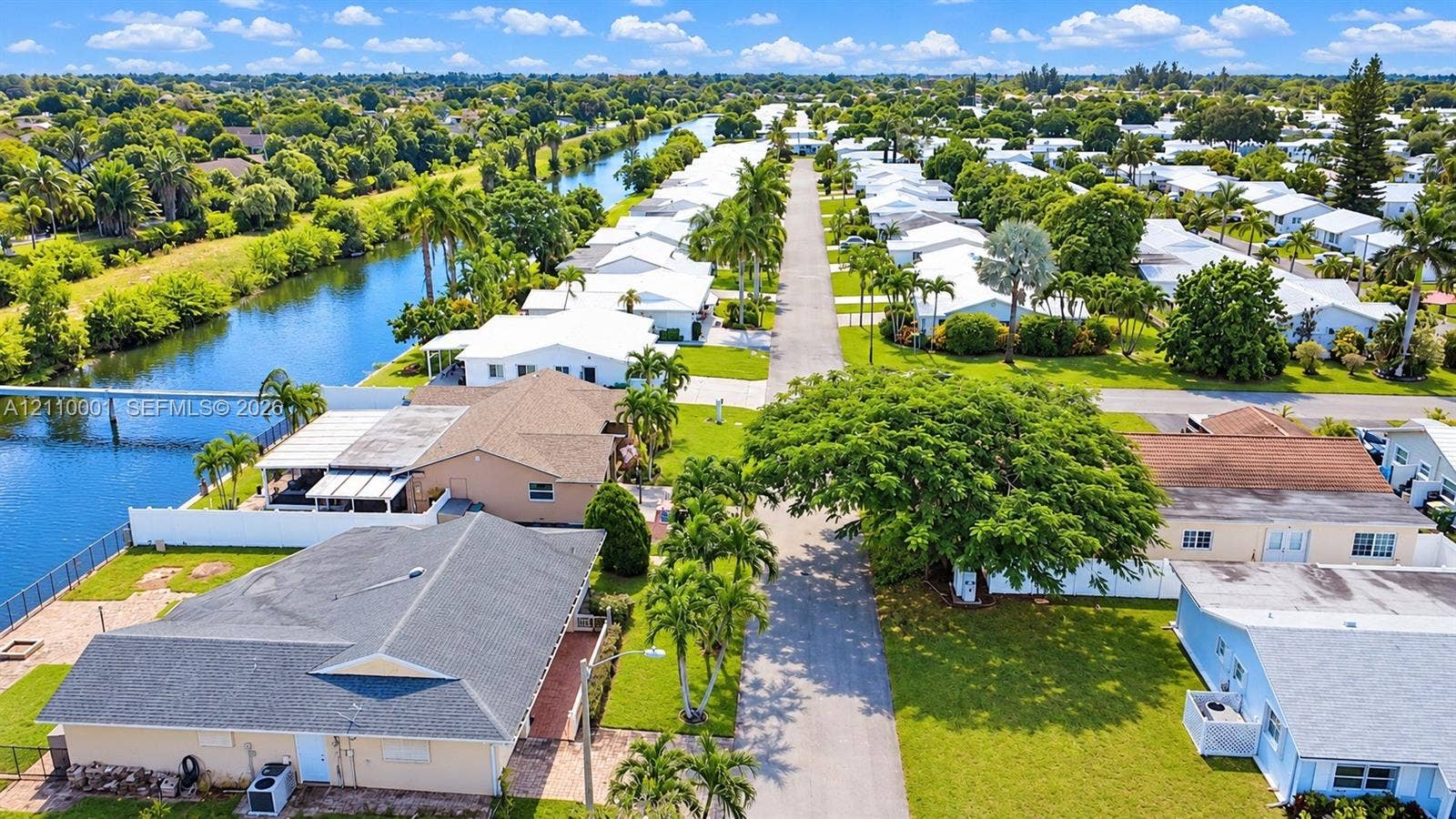 3617 SW 69th Terrace, #24-Z, Miramar, FL 33023 Aerial perspective of a residential street featuring waterfront access, paved thoroughfare, manicured landscaping, mature canopy trees, and established perimeter fencing