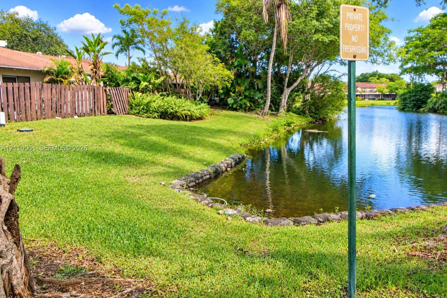 3617 SW 69th Terrace, #24-Z, Miramar, FL 33023 Waterfront lot featuring a natural grass lawn, stone-lined bulkhead, mature trees, and wooden perimeter fencing