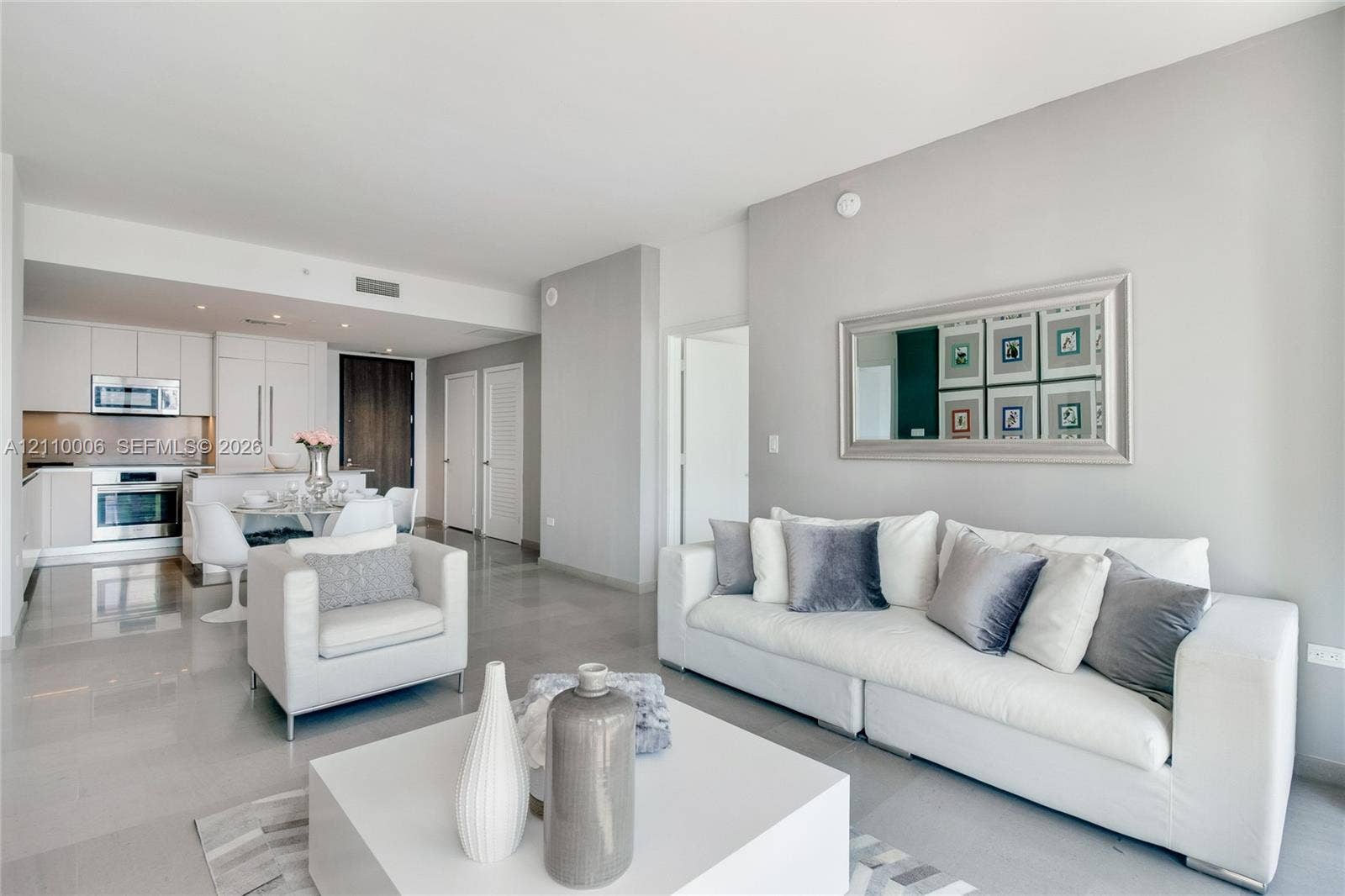 Open-concept interior featuring light-toned tile flooring, recessed ceiling lighting, and a modern kitchen with flat-panel cabinetry and stainless-steel appliances