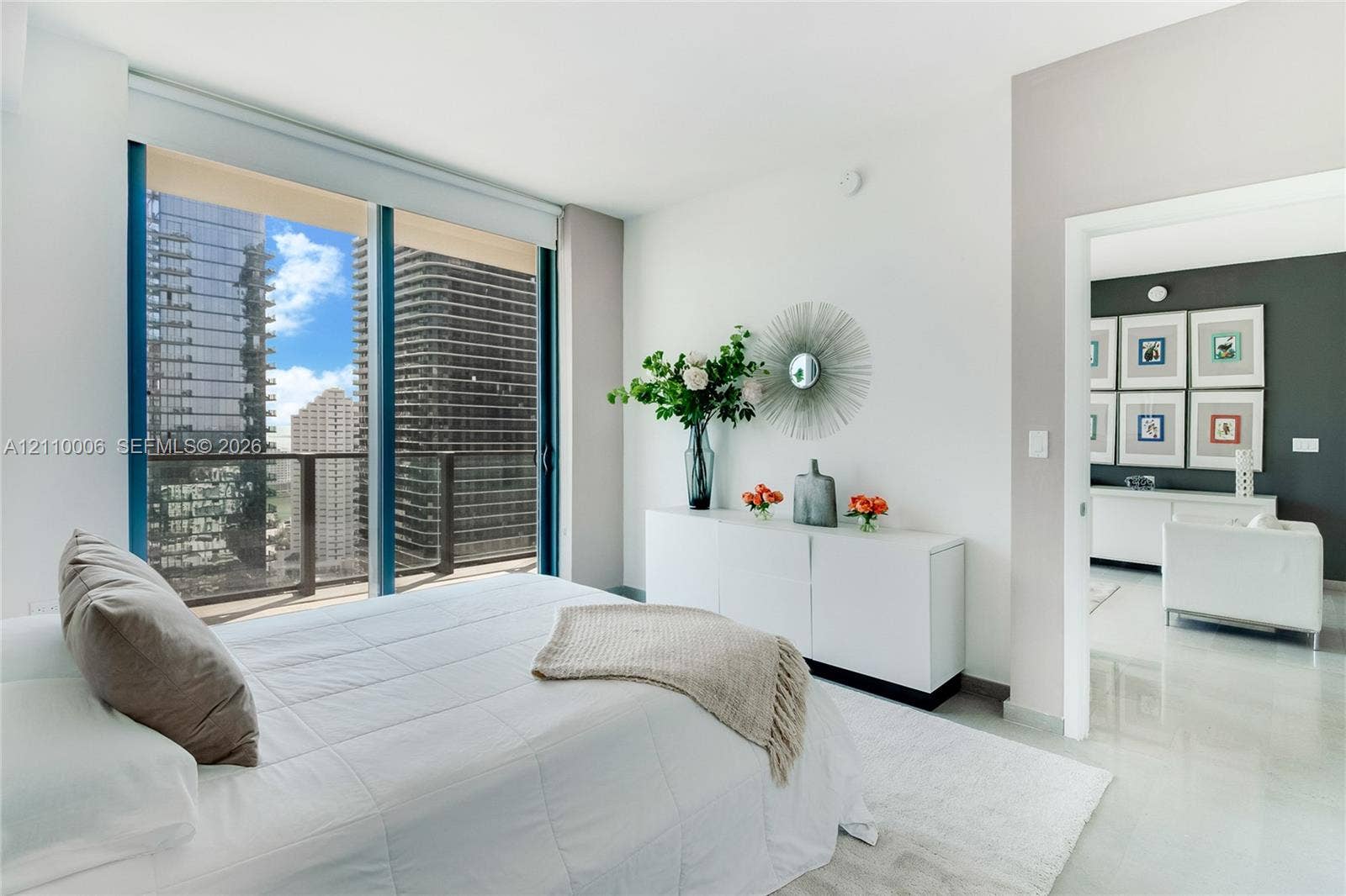 Floor-to-ceiling windows featuring urban scenery, sliding glass door with balcony access, and polished stone flooring