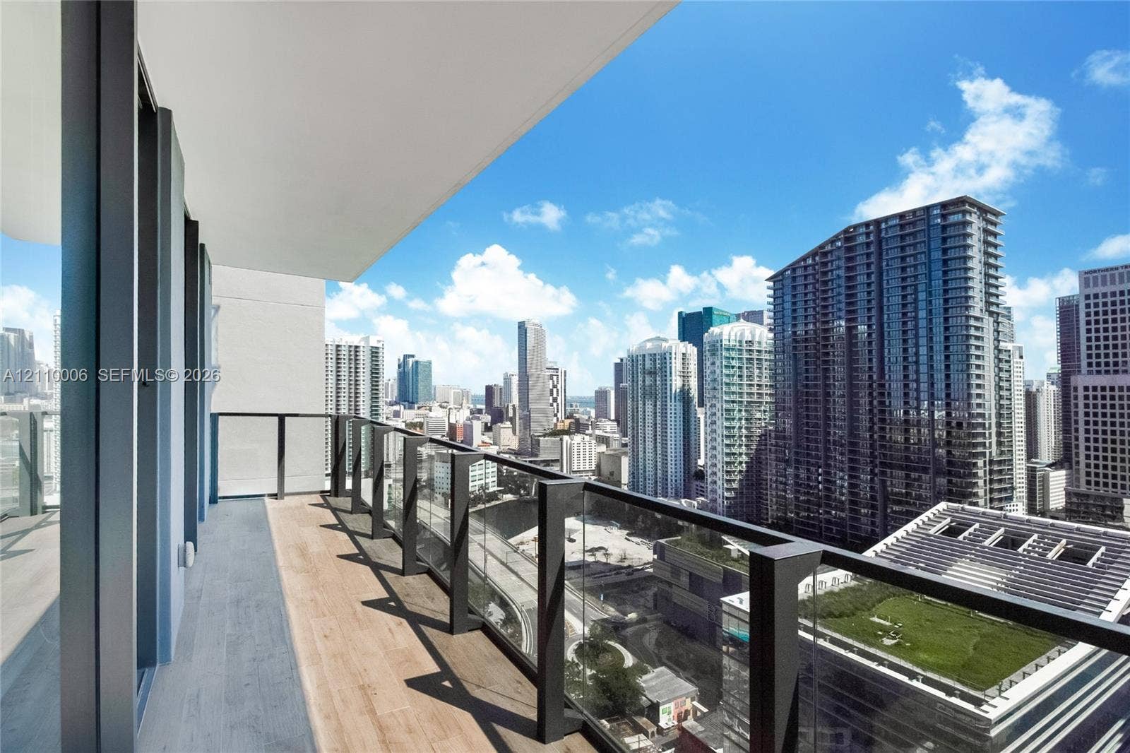 Covered balcony featuring wood-finish flooring, black metal frame, and glass pane railing with expansive city skyline exposure