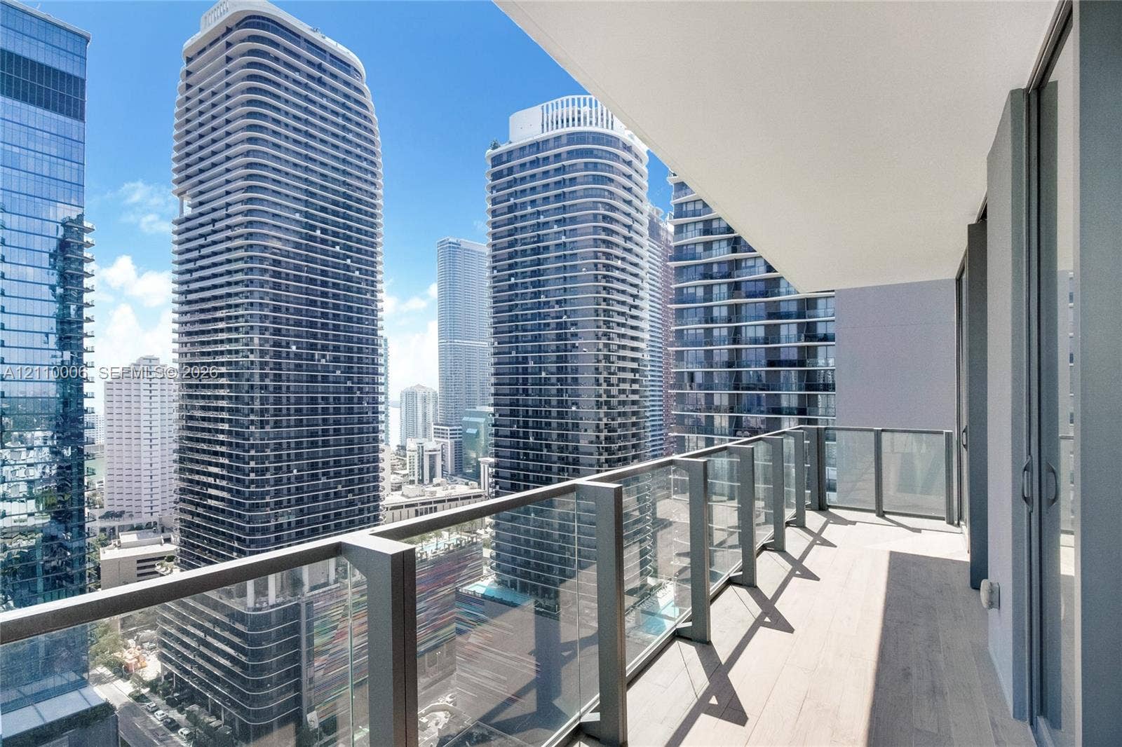 Private balcony with light-toned wood-finish flooring, glass panel railings, and metal framing