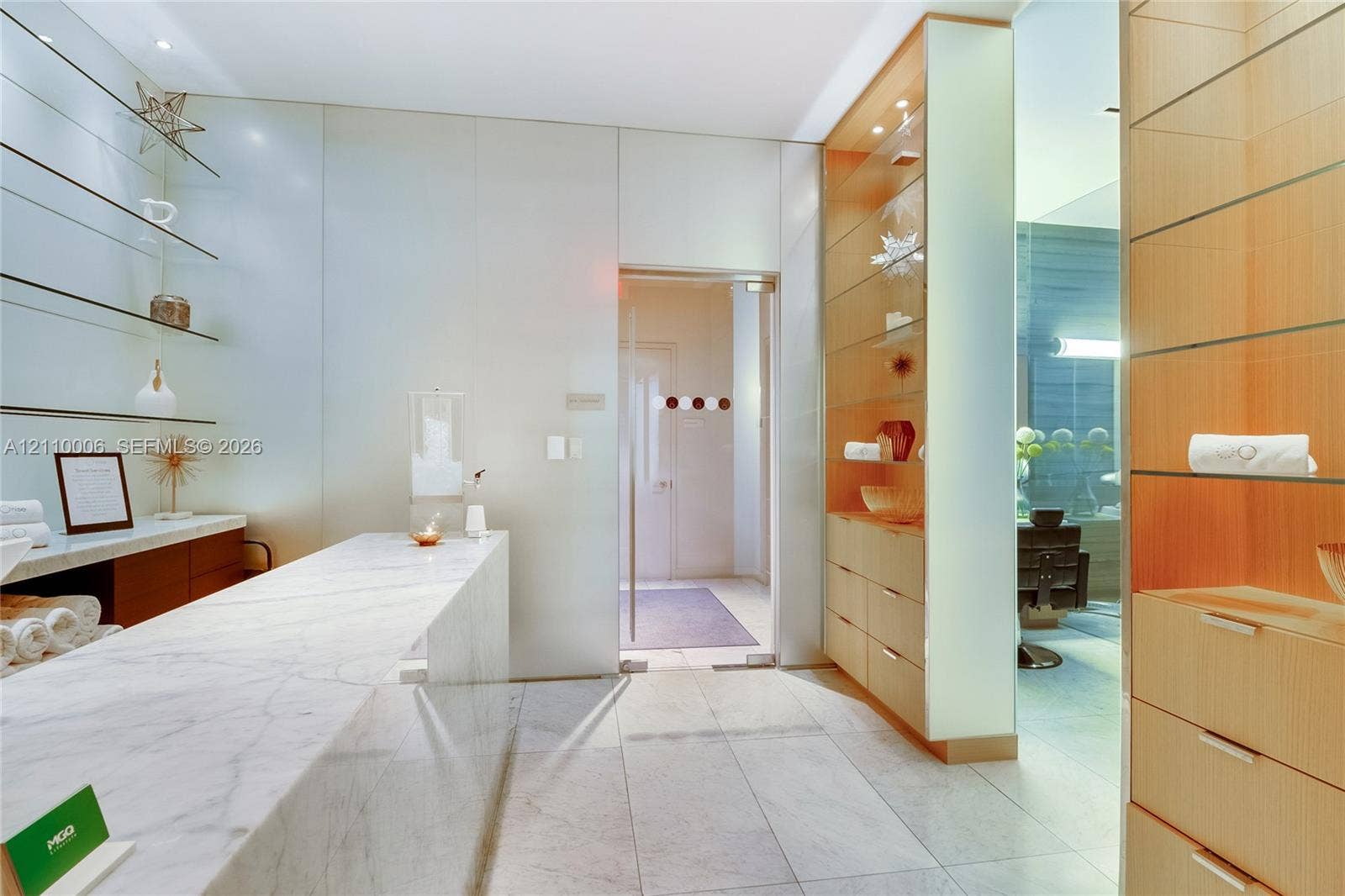 Custom built-in wood cabinetry, integrated glass shelving, stone countertop, stone tile flooring, and a glass-paneled entry door