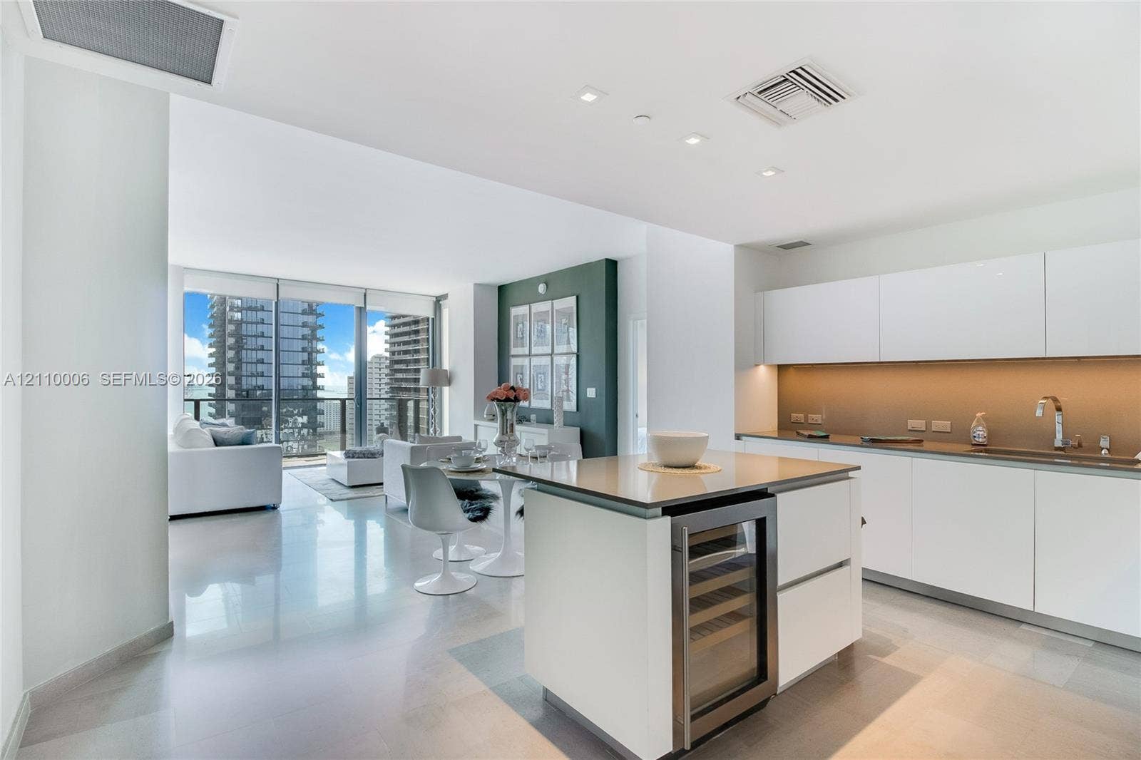 Modern kitchen featuring high-gloss white cabinetry, integrated stainless steel appliances, built-in wine cooler, stone-finish countertops, and polished large-format flooring