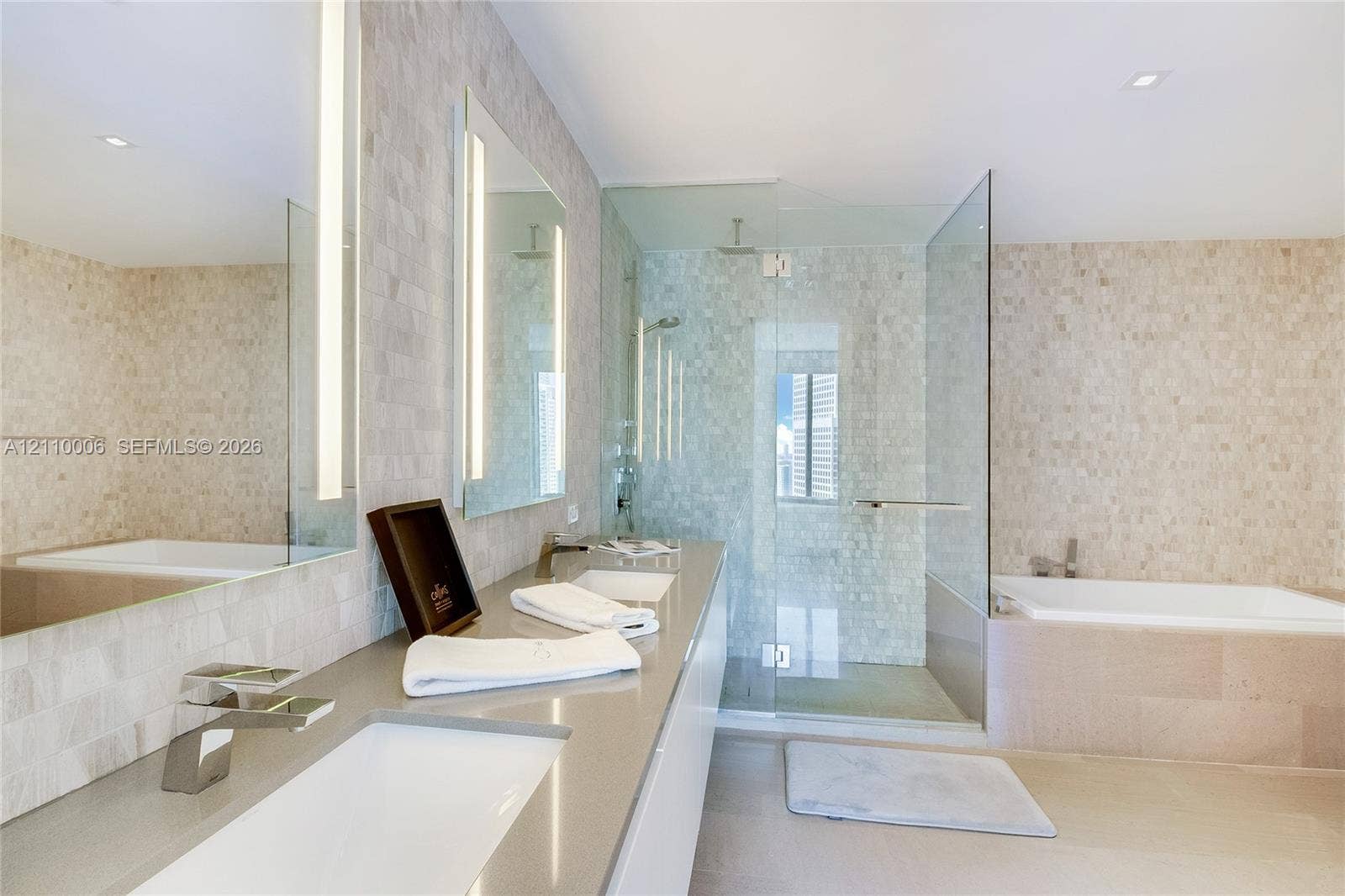 Dual-sink vanity with quartz countertops, integrated lighting in oversized mirrors, glass-enclosed shower, and a built-in soaking tub featuring stone-tile surround