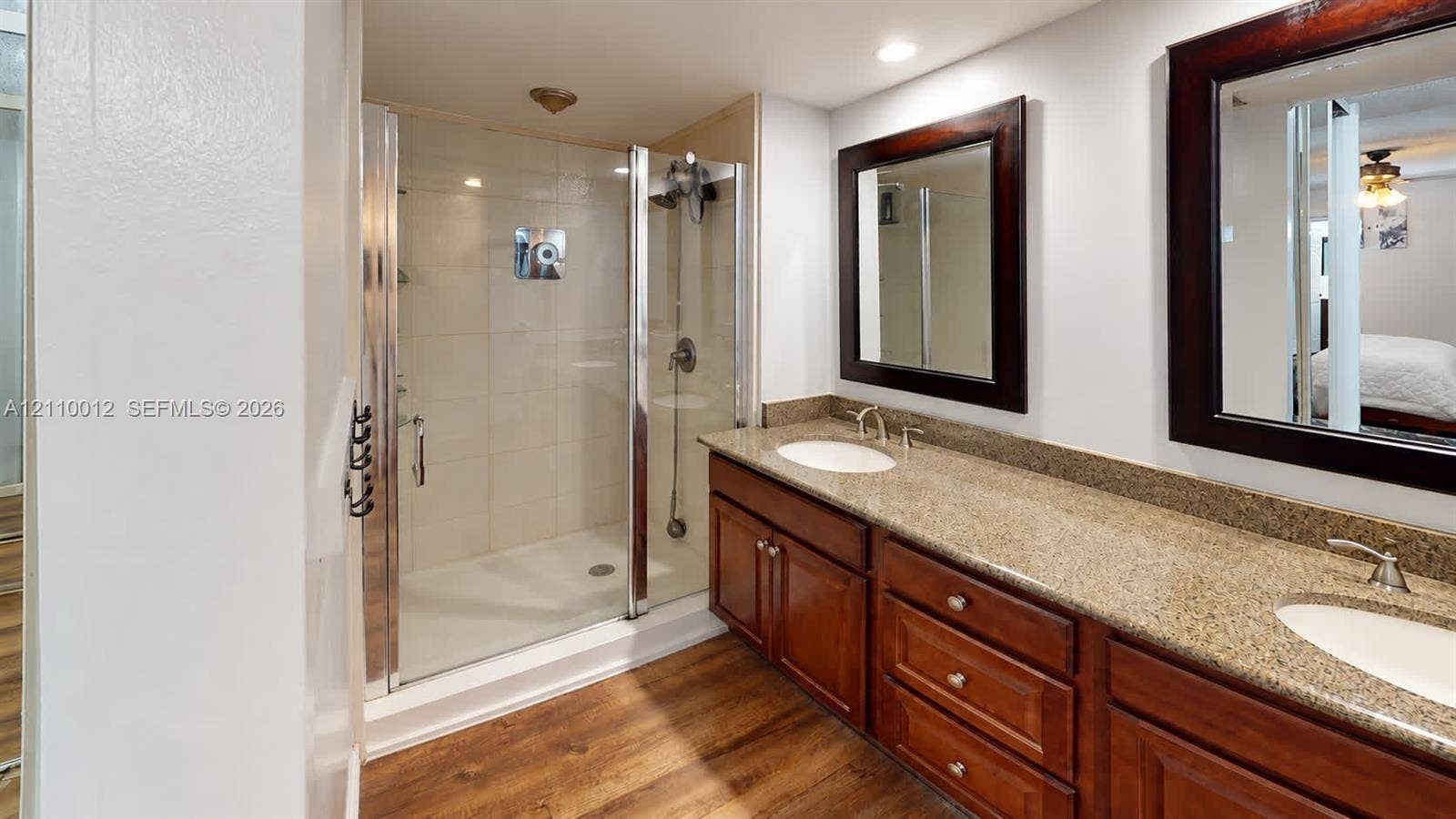 1601 16th Terrace, Palm Beach Gardens, FL 33418 Dual-sink vanity with stone-finish countertop and wood-finish cabinetry, frameless glass shower enclosure with tiled walls, and wood-finish flooring