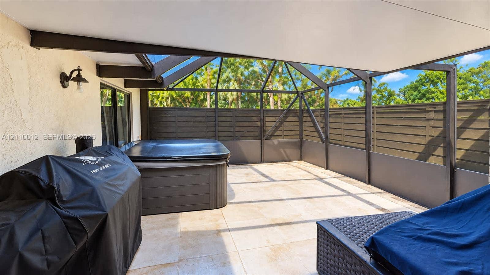 1601 16th Terrace, Palm Beach Gardens, FL 33418 Screened-in patio featuring tiled flooring, a built-in spa, privacy fencing, and a wall-mounted exterior light fixture