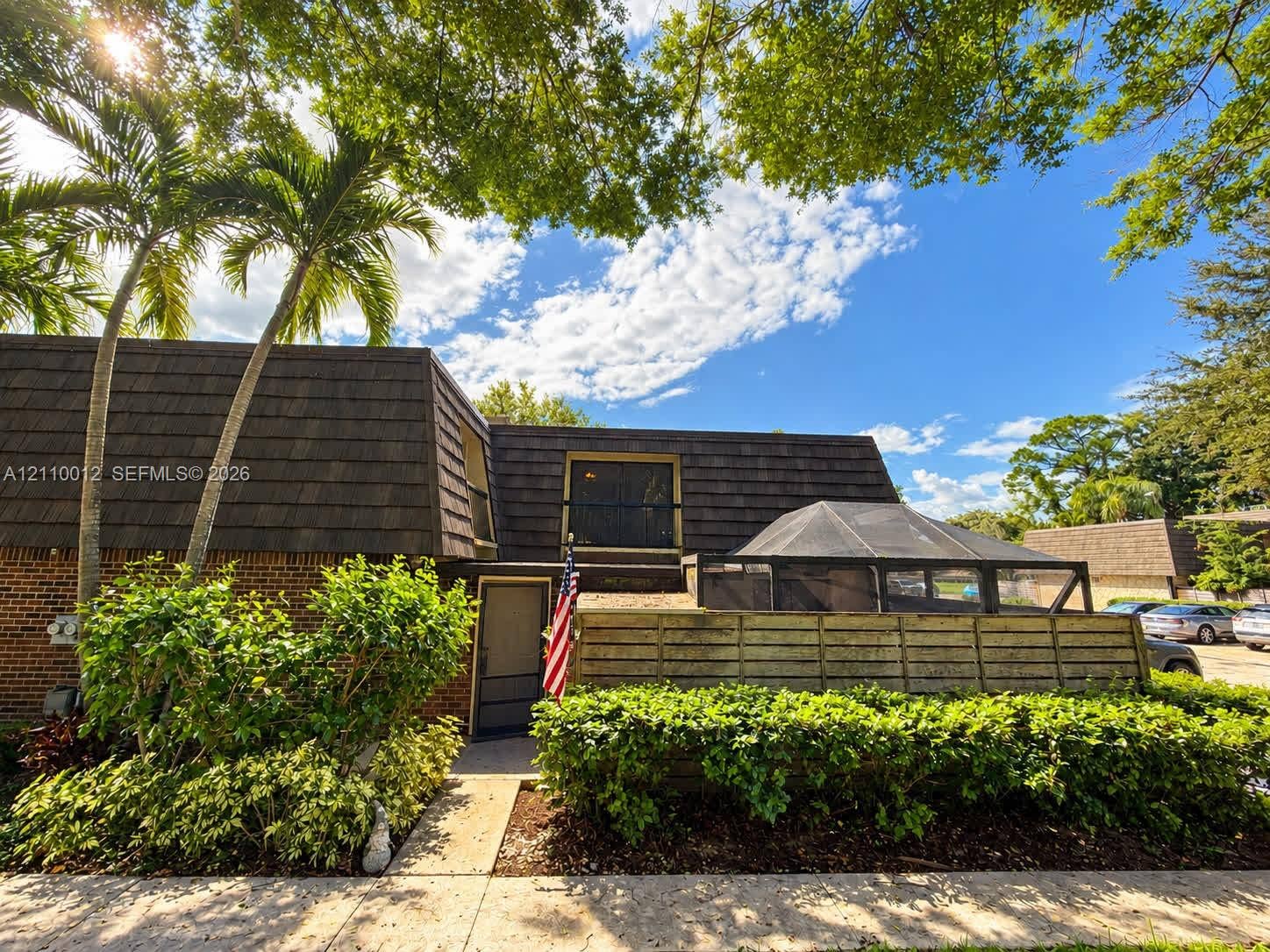 1601 16th Terrace, Palm Beach Gardens, FL 33418 Exterior featuring brick masonry, dark shingled mansard roofline, screened-in enclosure, and mature landscaping