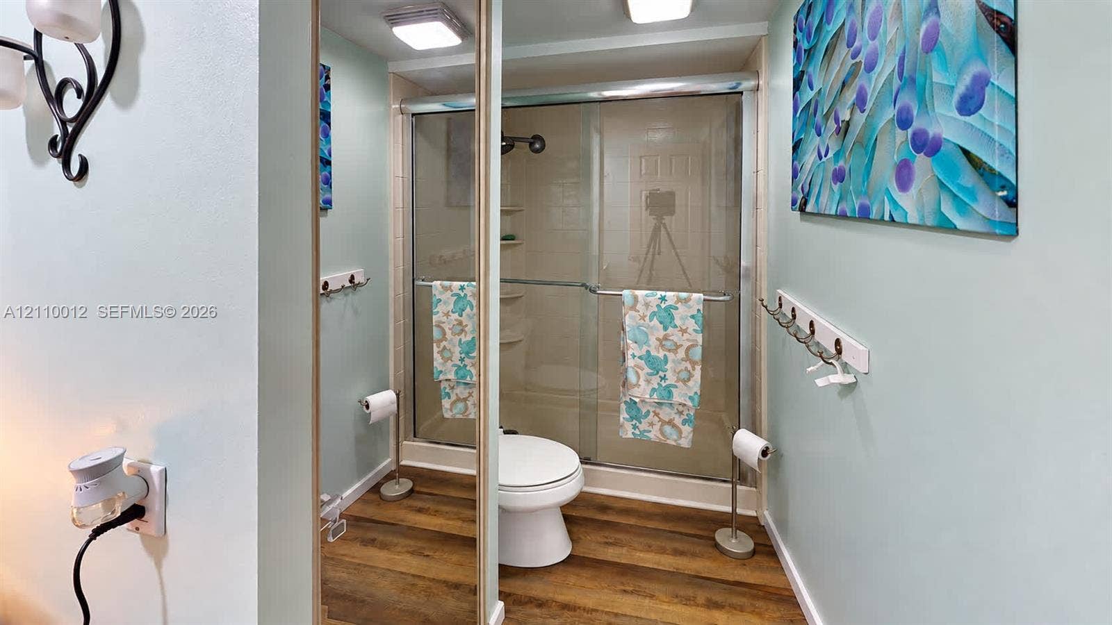 1601 16th Terrace, Palm Beach Gardens, FL 33418 Bathroom featuring wood-finish flooring, a glass-enclosed shower, a wall-mounted hook rack, and overhead lighting
