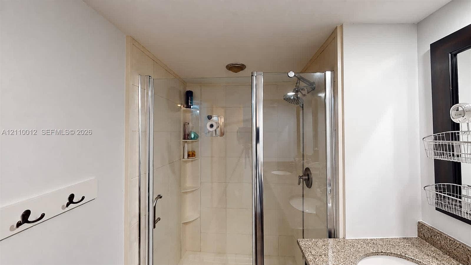 1601 16th Terrace, Palm Beach Gardens, FL 33418 Walk-in shower featuring a frameless glass door, neutral-toned wall tile, and integrated corner shelving, complemented by a vanity with a stone-finish countertop