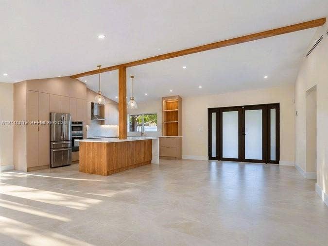 1708 SW 11th Street, Fort Lauderdale, Fort Lauderdale, FL 33312 Open-concept interior featuring vaulted ceilings with exposed wood beams, large-format tile flooring, a kitchen island with wood-finish cabinetry, built-in floor-to-ceiling cabinetry, and French doors