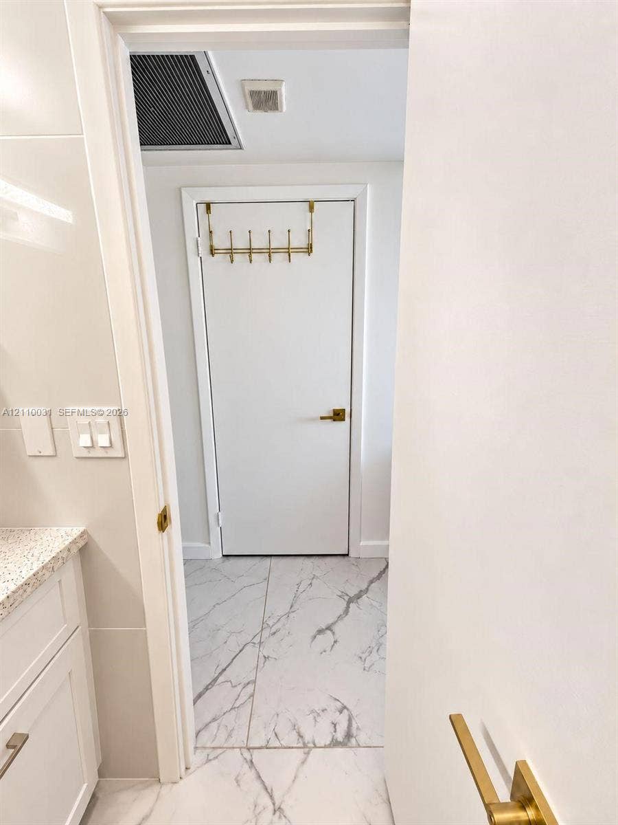 Stone-finish tile flooring, white cabinetry with stone-finish countertop, and brass-tone hardware