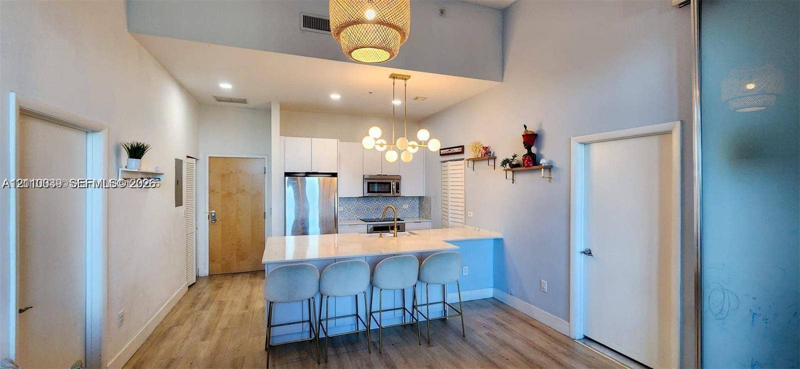 244 Biscayne Boulevard, #301, Miami, FL 33132 Modern kitchen featuring white flat-panel cabinetry, light-toned stone-surface island, stainless steel appliances, tiered globe chandelier, and light wood-finish flooring
