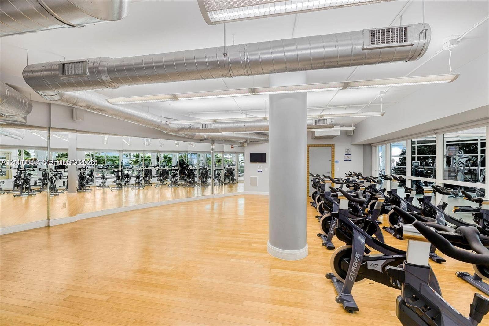 244 Biscayne Boulevard, #301, Miami, FL 33132 Industrial aesthetic featuring exposed metal ductwork, full-wall mirrors, light wood-finish flooring, and linear LED lighting