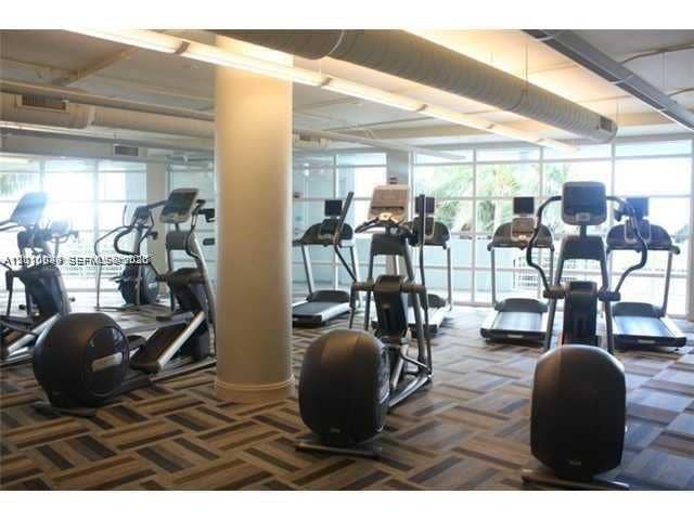 244 Biscayne Boulevard, #301, Miami, FL 33132 Fitness center featuring floor-to-ceiling windows, patterned modular carpeting, exposed structural support columns, and industrial-style overhead lighting