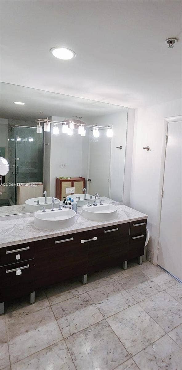 244 Biscayne Boulevard, #301, Miami, FL 33132 Double vanity featuring dark wood-finish cabinetry, a stone-style countertop, dual round drop-in sinks, and a large-format mirror with integrated overhead lighting